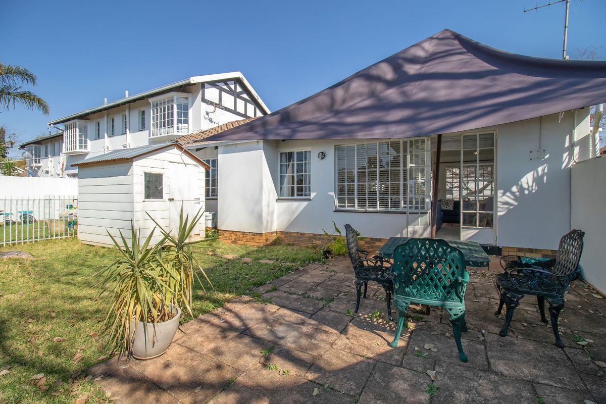 Rear view of the townhouse featuring a paved patio area, a small garden, and a detached storage shed.