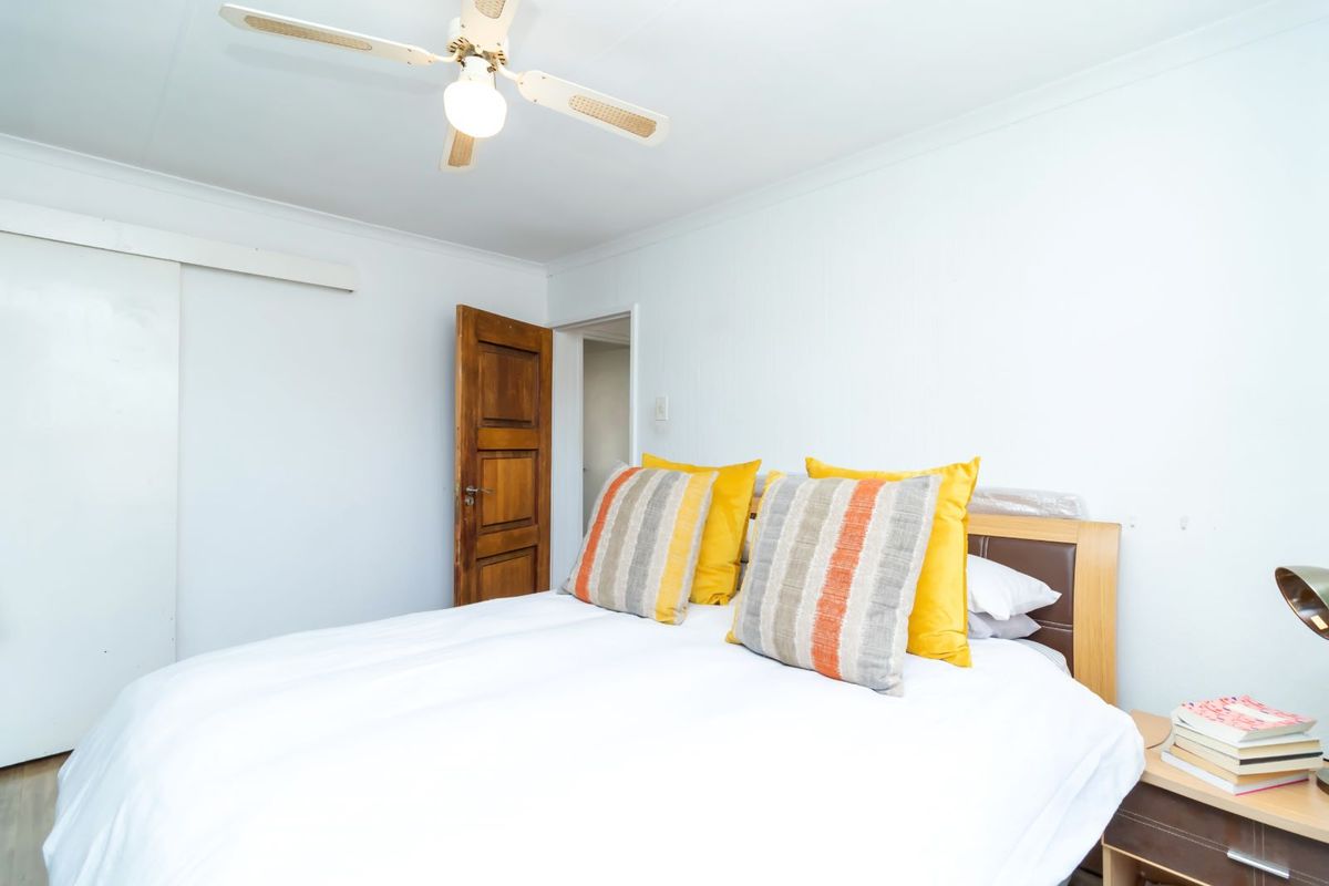 A functional bedroom featuring a ceiling fan, built-in sliding door wardrobe, and traditional wooden door, providing a simple and practical living space.
