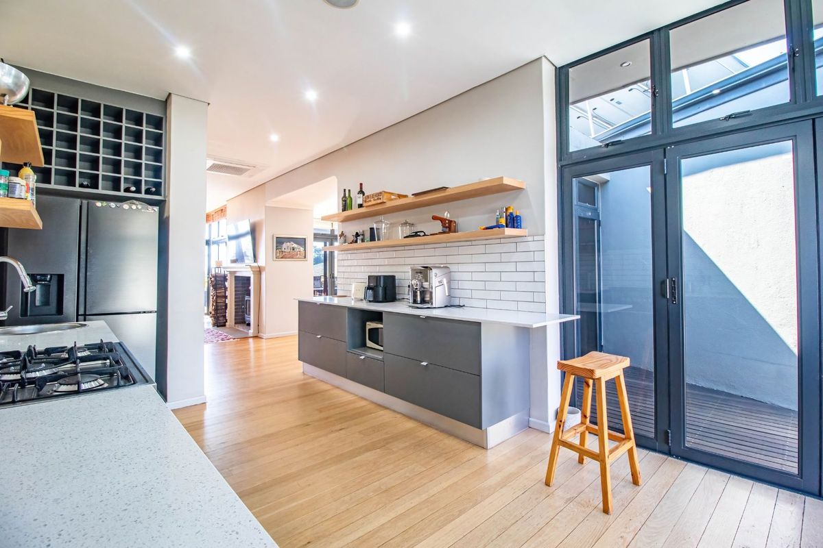 Modern kitchen featuring sleek grey cabinetry, stone countertops, subway tile backsplash, open timber shelving, and direct access to an outdoor courtyard area.
