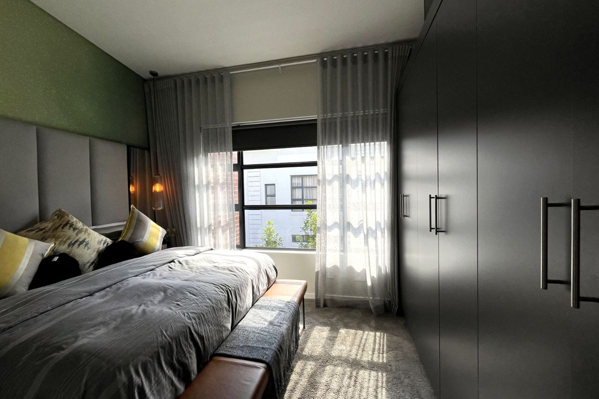 A well-appointed bedroom featuring built-in floor-to-ceiling cabinetry, plush carpeting, and a large window allowing for ample natural light.