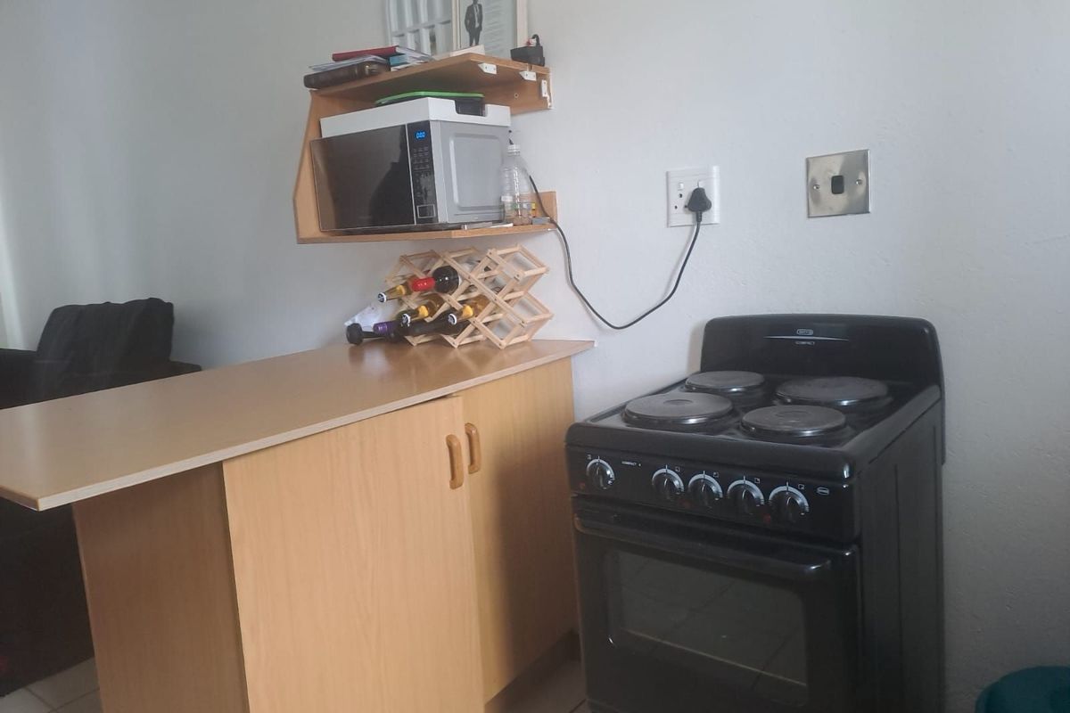 A compact kitchen area featuring a freestanding electric stove, built-in cabinetry, and a wall-mounted shelf for additional storage.