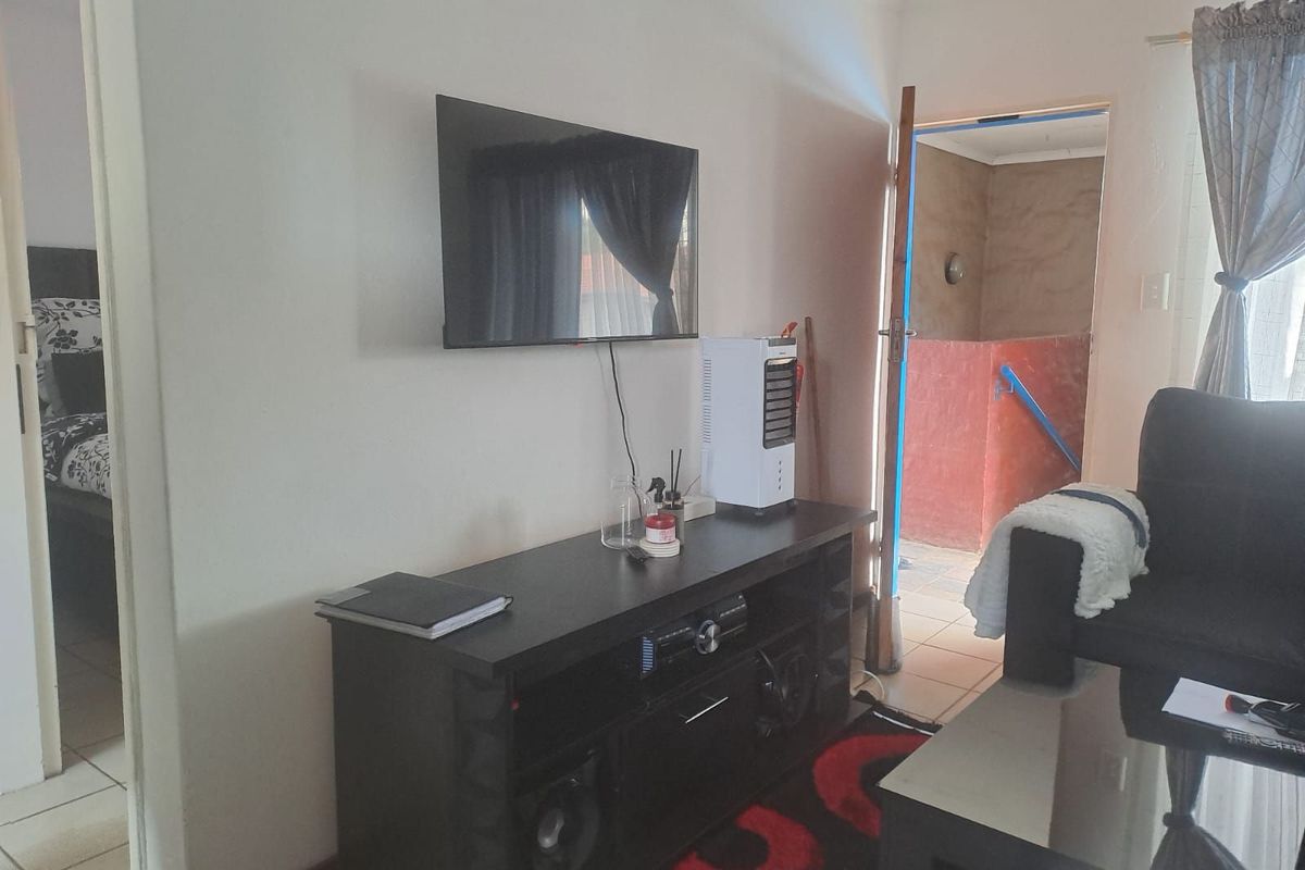A living room area featuring tiled flooring, neutral wall finishes, and direct access to an adjacent room and exterior space.