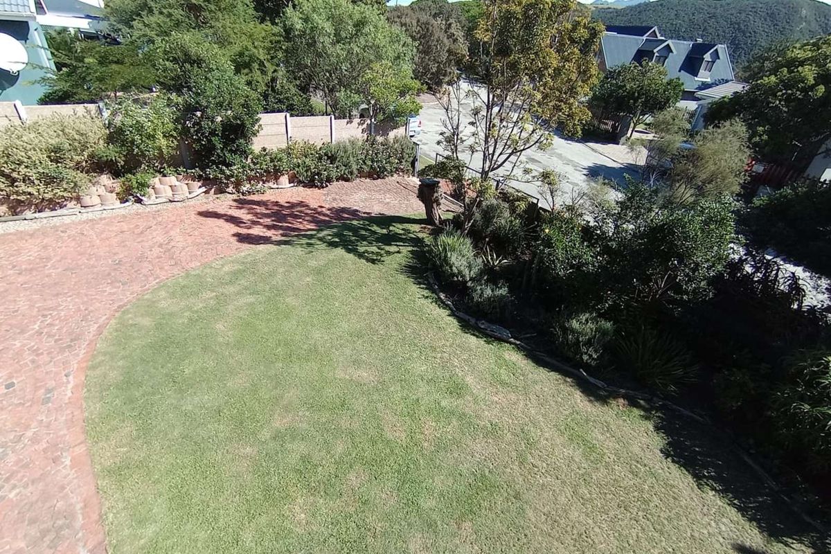 An elevated view of the front garden featuring a manicured lawn, established landscaping, and a paved driveway area.