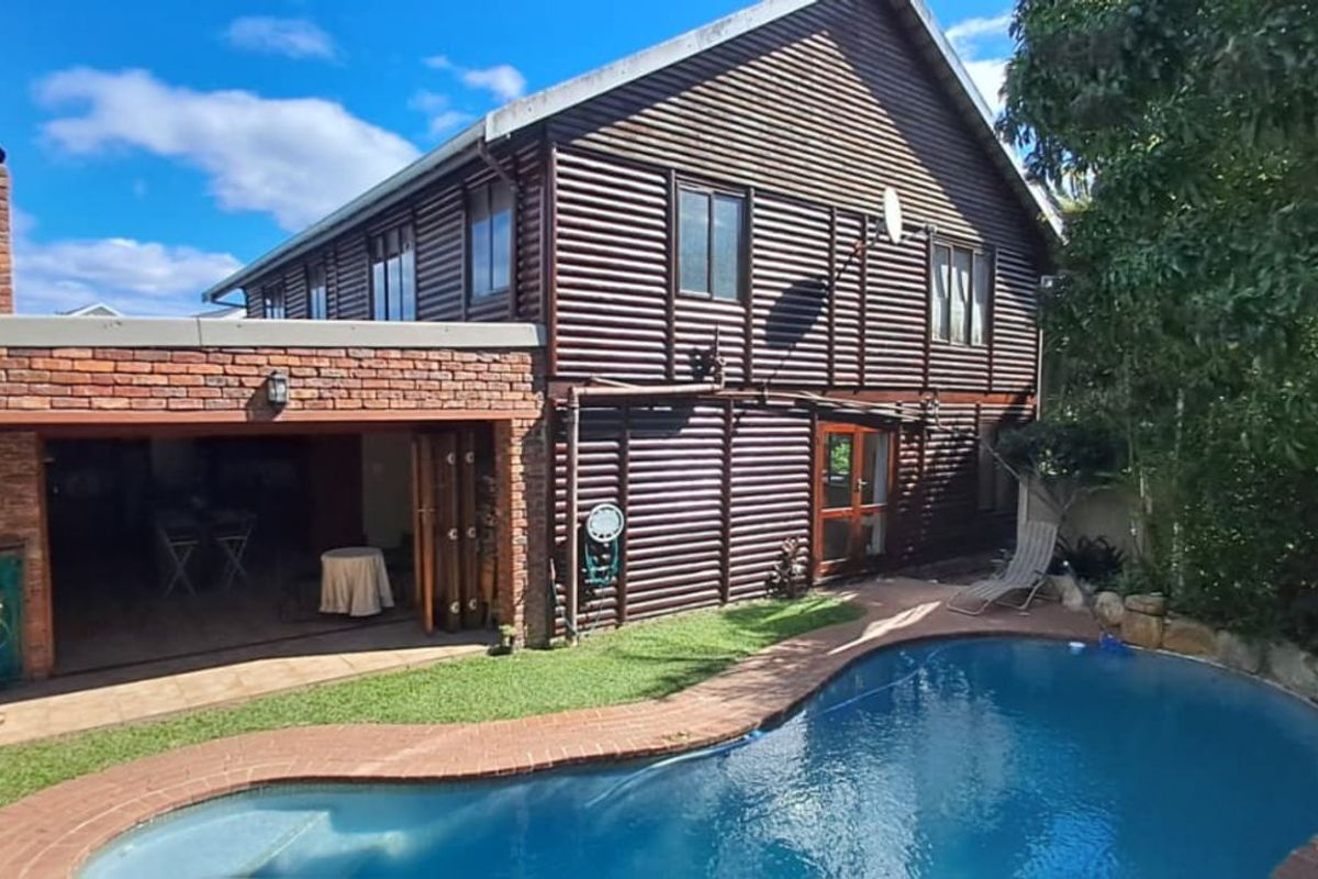 Rear view of the property featuring a swimming pool, brick-built patio area, and timber-clad exterior walls.