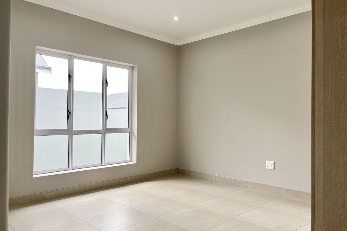 A bright, empty bedroom featuring neutral wall paint, large windows, and modern tiled flooring with matching skirting boards.