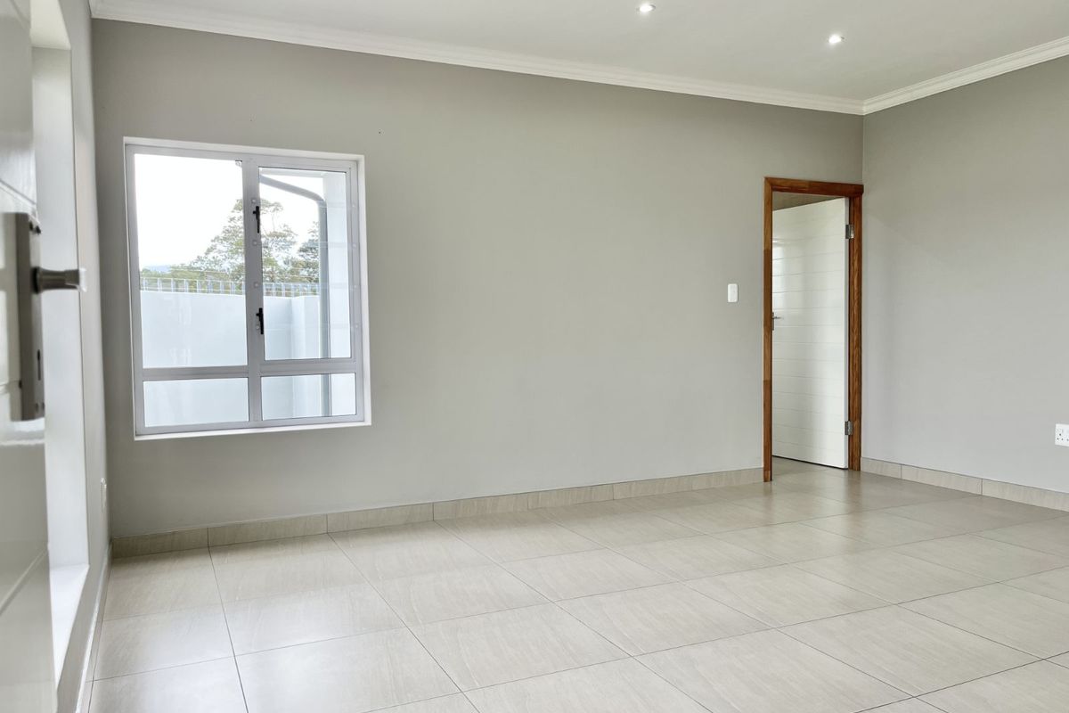 A bright, neutral-toned living area featuring large format floor tiles, recessed downlighting, and a clean, modern finish.