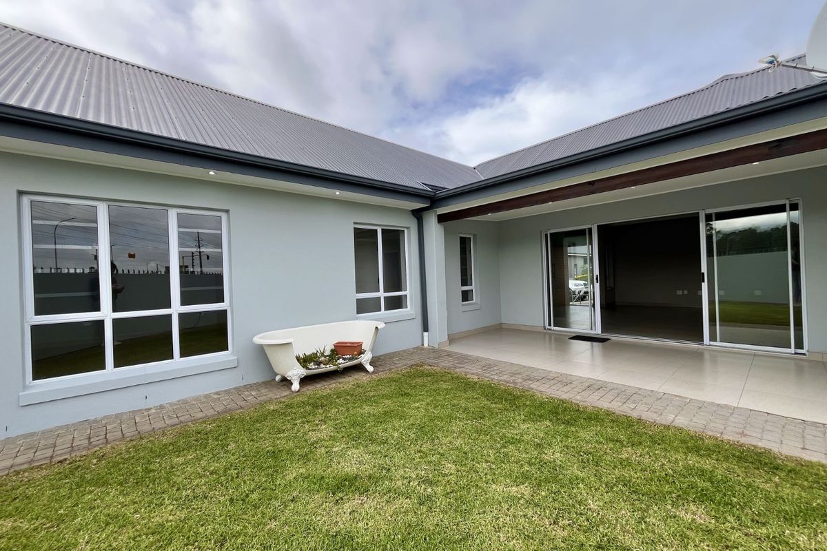 A view of the rear exterior featuring a covered patio with tiled flooring, sliding glass doors, and a well-maintained lawn area.
