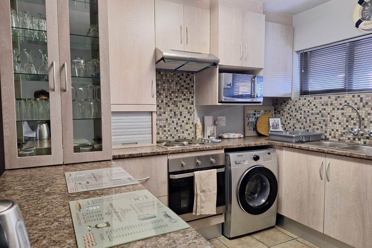 Compact kitchen featuring light wood-grain cabinetry, mosaic tile backsplash, granite-look countertops, built-in oven, hob, extractor fan, and integrated laundry appliance space.