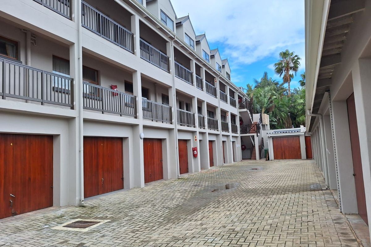 Exterior view of an apartment complex featuring a paved driveway, multiple garage units, and multi-level balconies with metal railings.