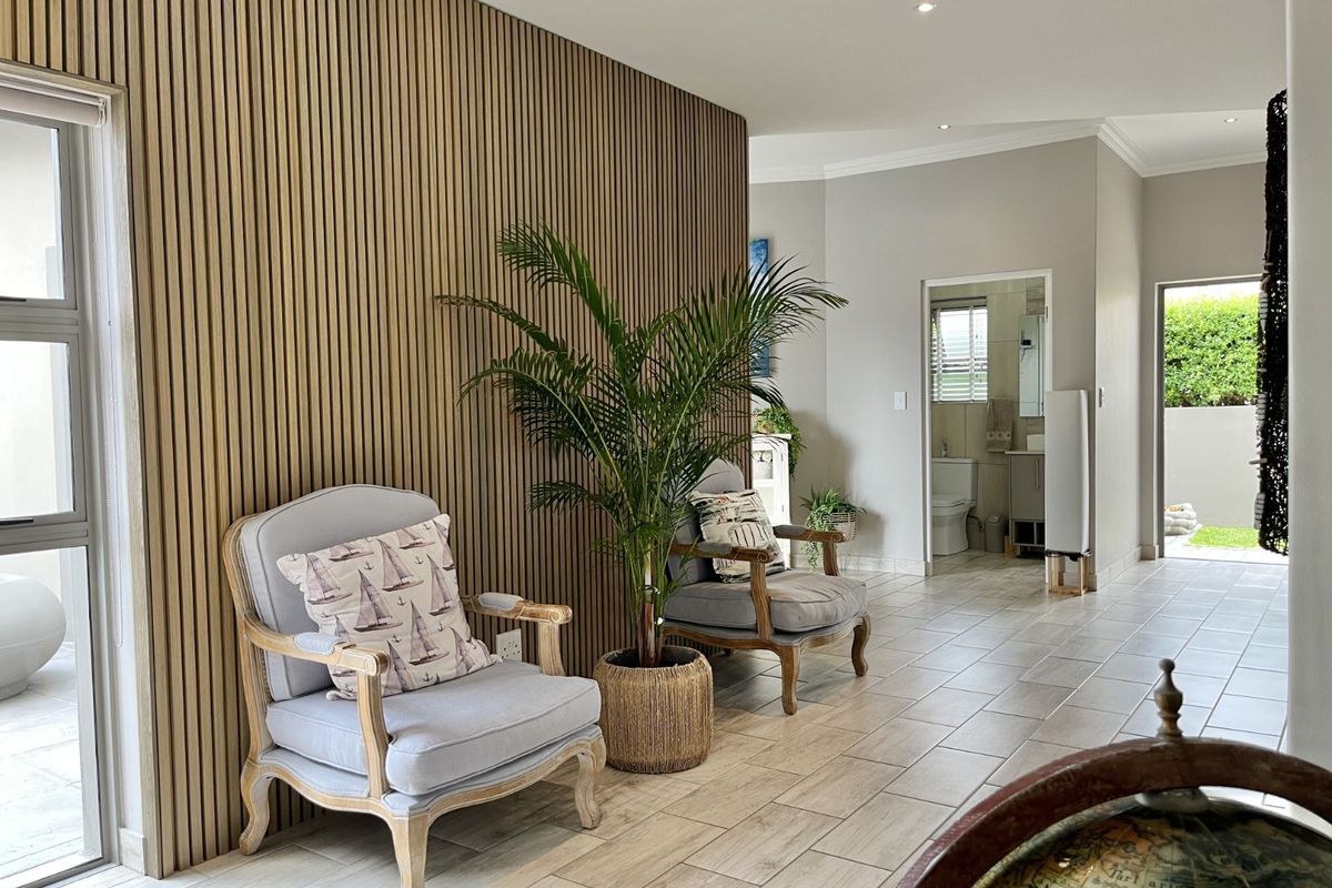 A bright living area featuring a modern timber slat feature wall, tiled flooring, and recessed downlighting, with a view into an adjacent bathroom.