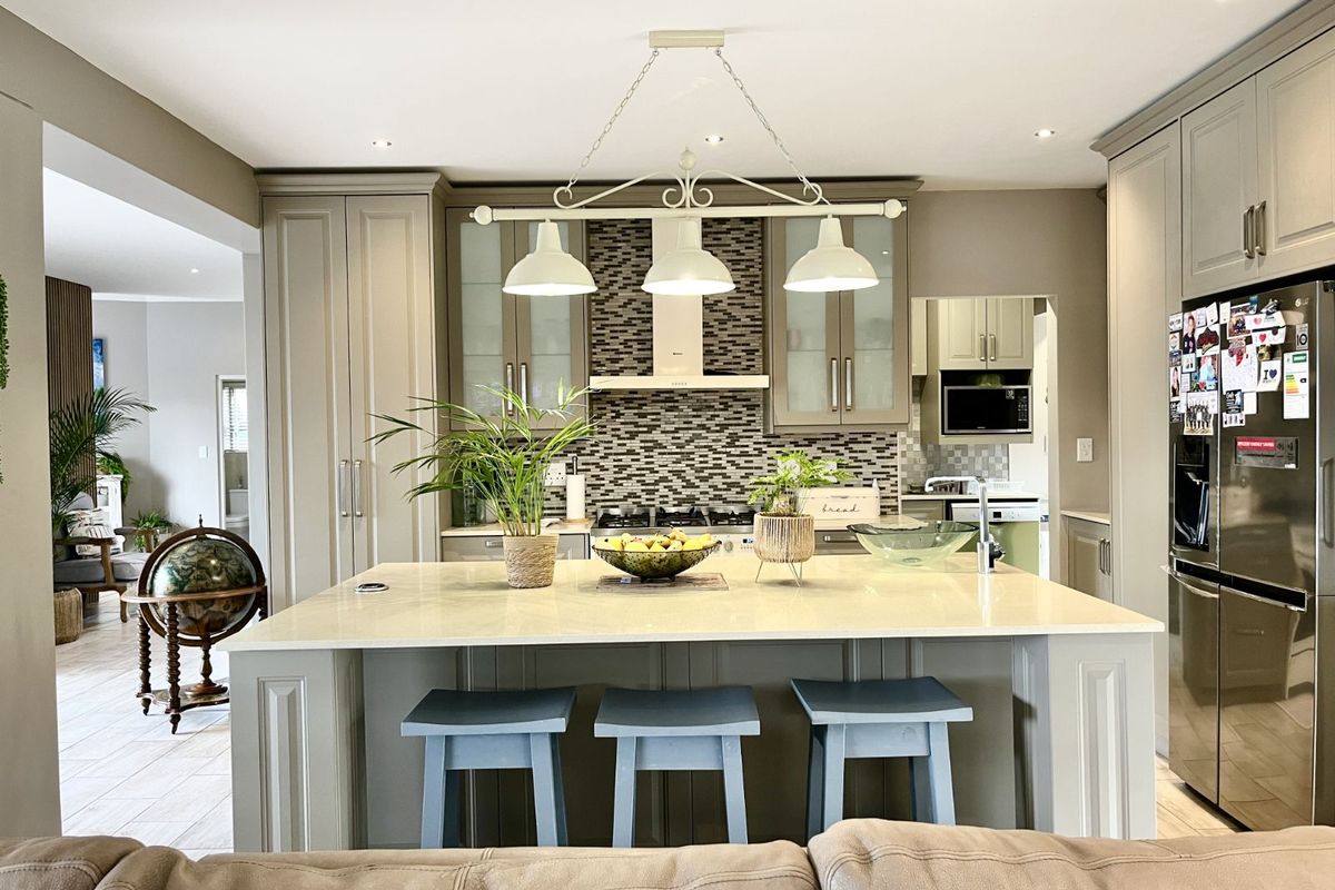 Modern kitchen featuring a large central island with stone countertop, shaker-style cabinetry, mosaic tile backsplash, and integrated stainless steel appliances.