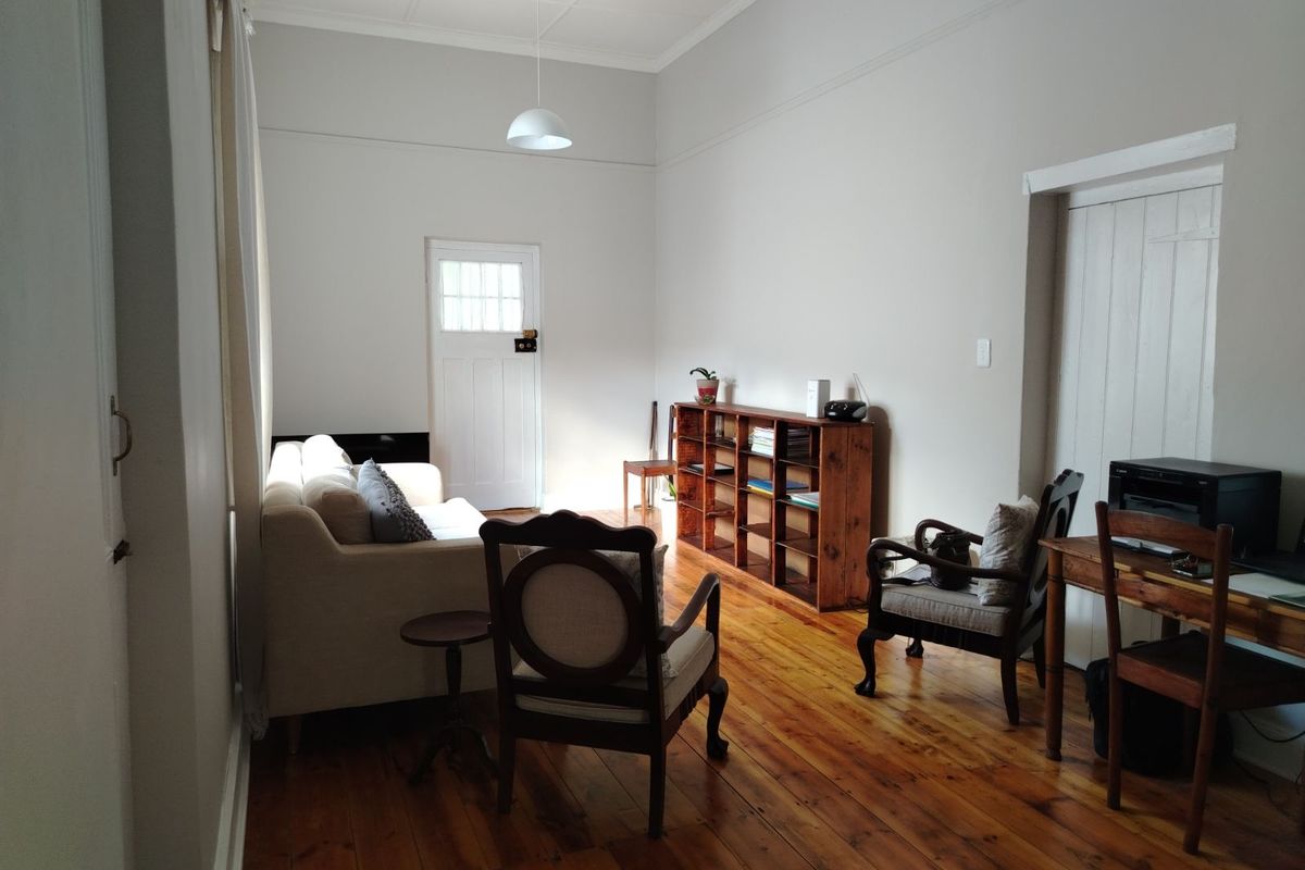 A living room featuring original timber flooring, high ceilings with decorative cornicing, and a classic panelled door leading to the exterior.
