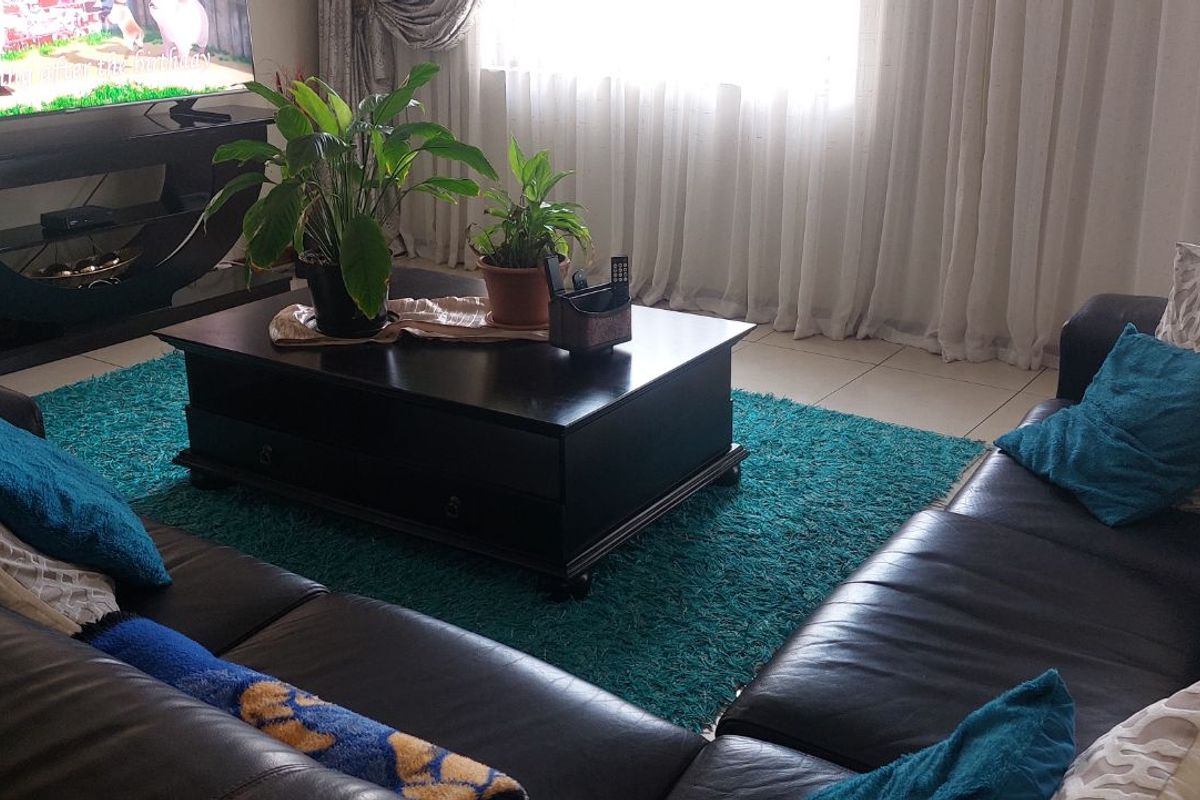 A comfortable living room featuring tiled flooring and large windows with curtains, providing a bright and inviting space for relaxation.