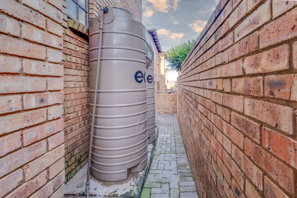 Side passage of the property featuring brick paving and two large plastic water storage tanks installed against the exterior brick wall.