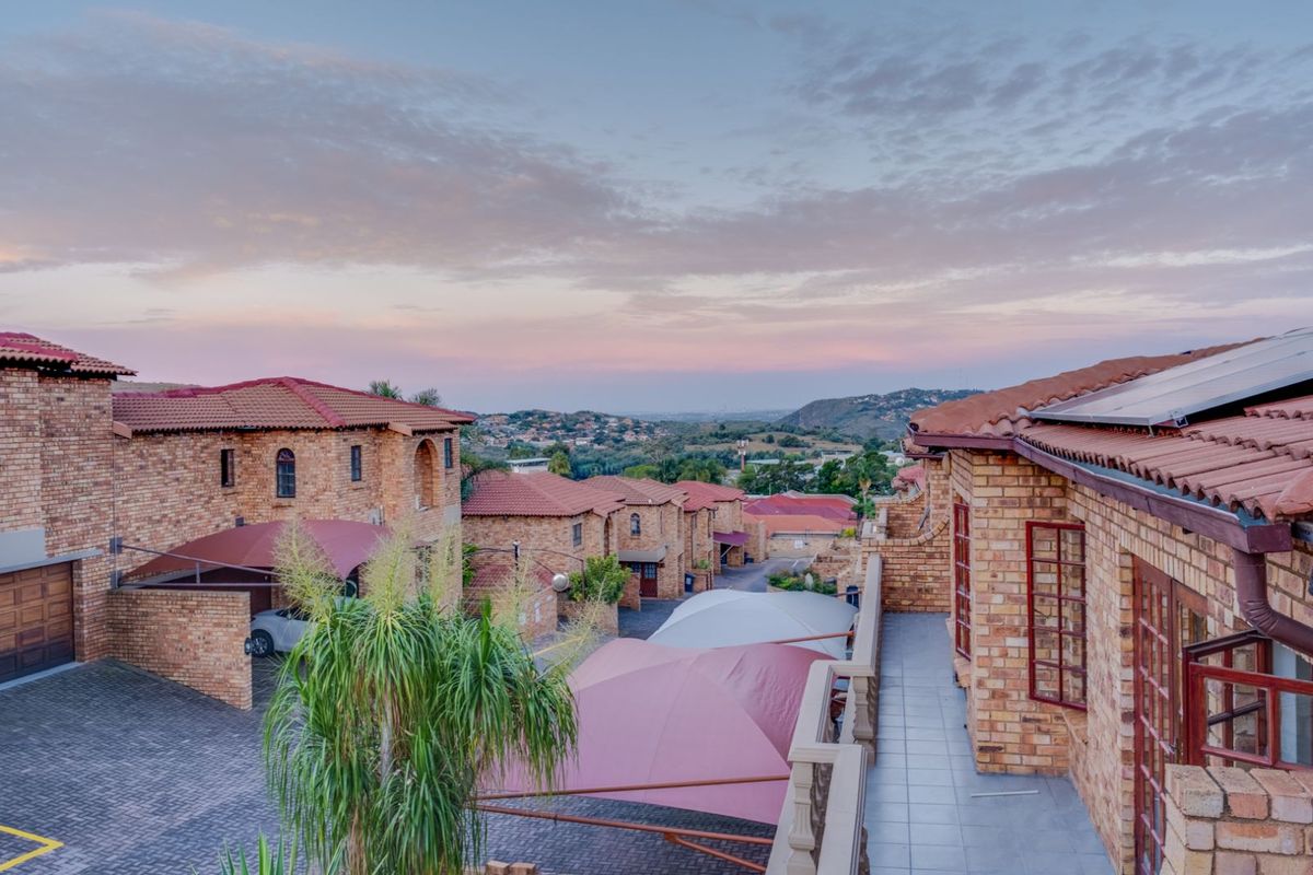 Elevated view of a residential estate featuring face-brick architecture, tiled roofing, solar panels, and paved driveways with shade-cloth carports at sunset.