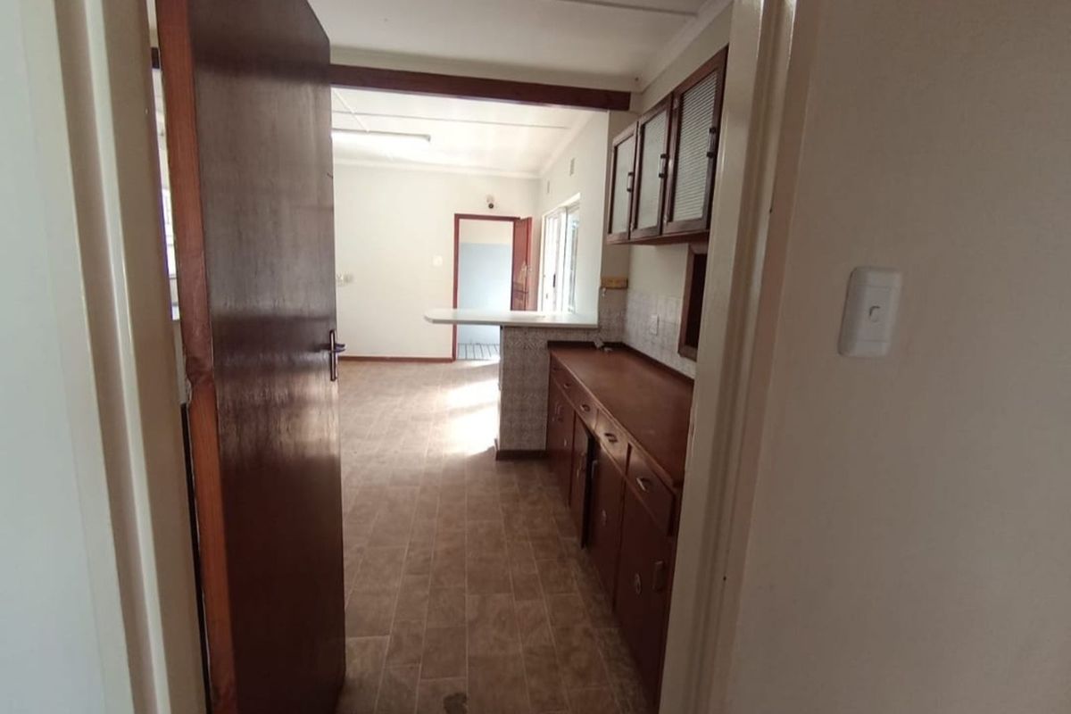 A view into a dated kitchen featuring wooden cabinetry, a breakfast bar, and tiled flooring, leading through to an adjacent living area.