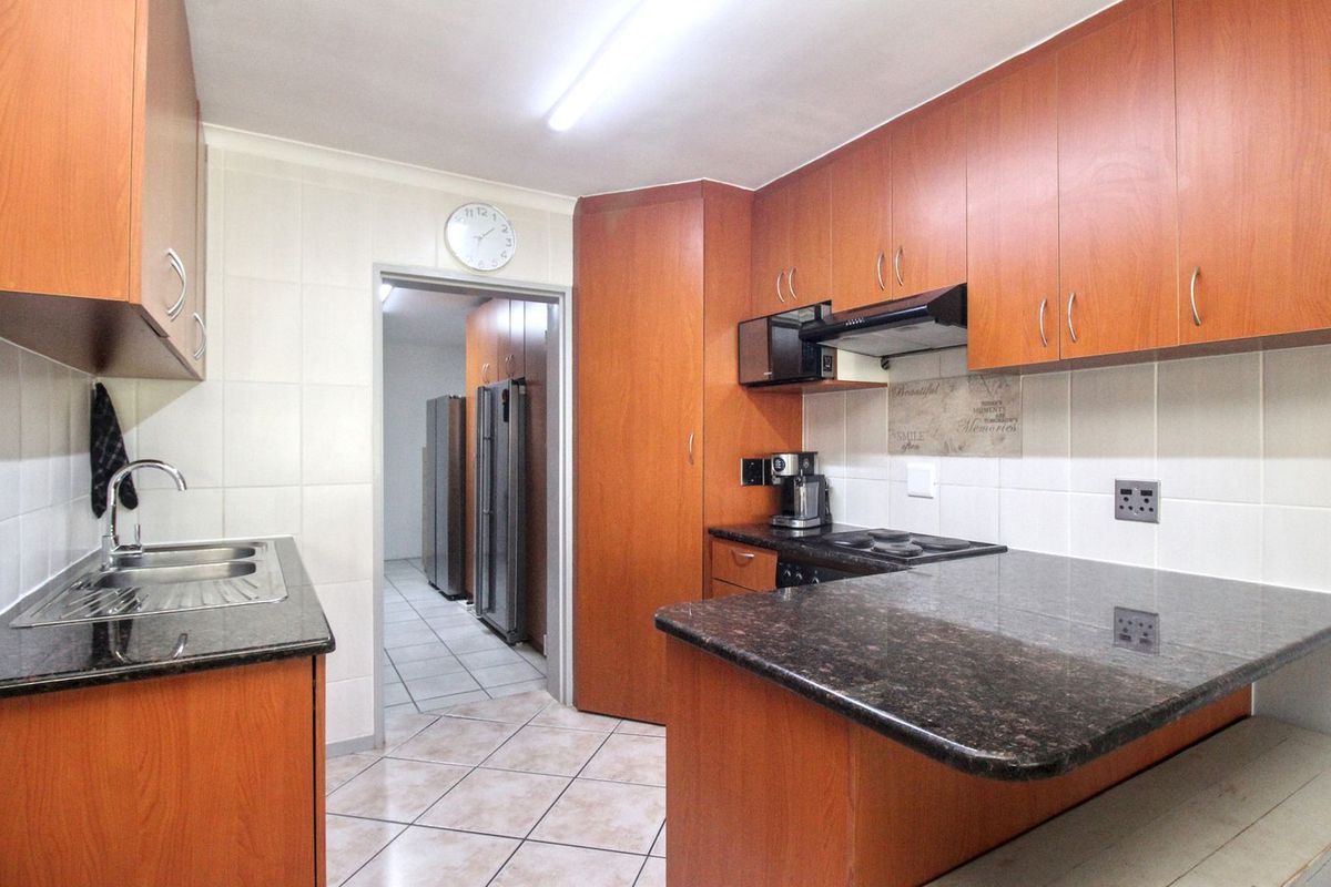 A functional kitchen featuring wood-finish cabinetry, granite countertops, a built-in hob, and an extractor fan, with an adjacent scullery area.