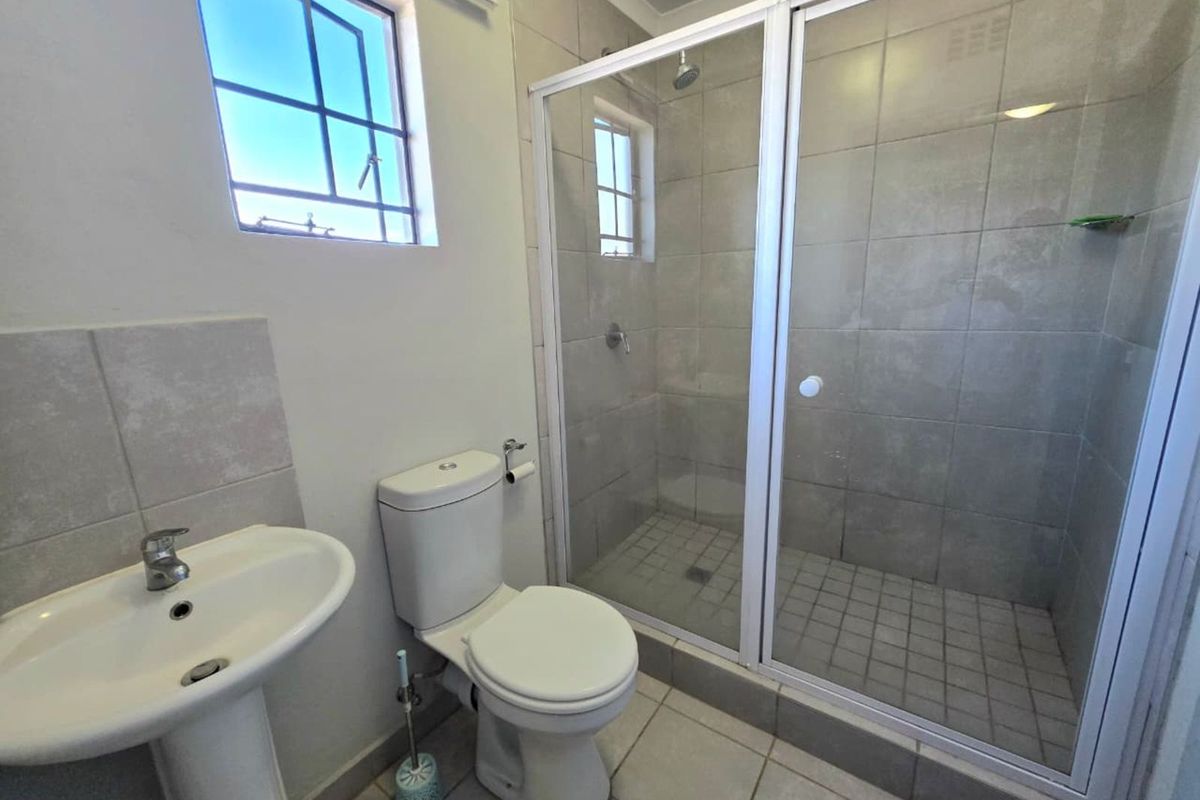A functional bathroom featuring a pedestal basin, a standard toilet, and a walk-in shower enclosure with tiled walls and flooring.
