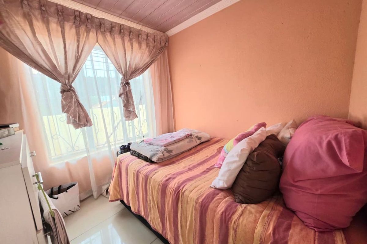 A compact bedroom featuring tiled flooring, a large window with curtains, and a painted ceiling.