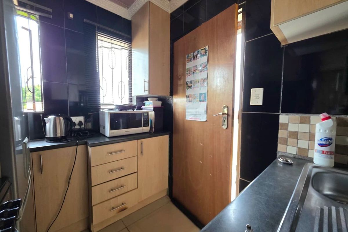 A functional kitchen featuring light wood cabinetry, dark countertops, and black wall tiling, providing a compact and practical workspace.