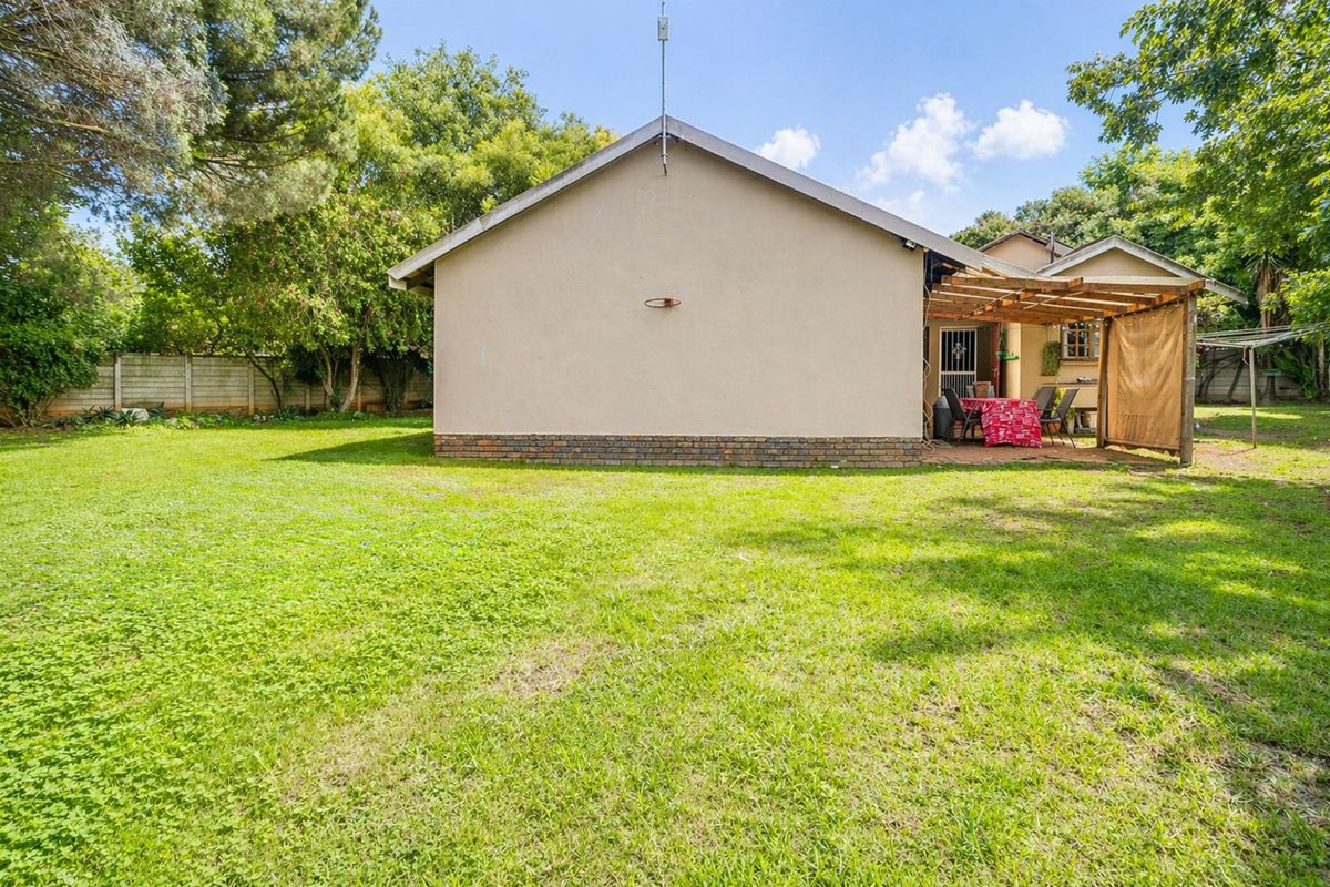 Rear view of the property featuring a spacious lawn, a brick-based exterior wall, and a timber-framed patio area.