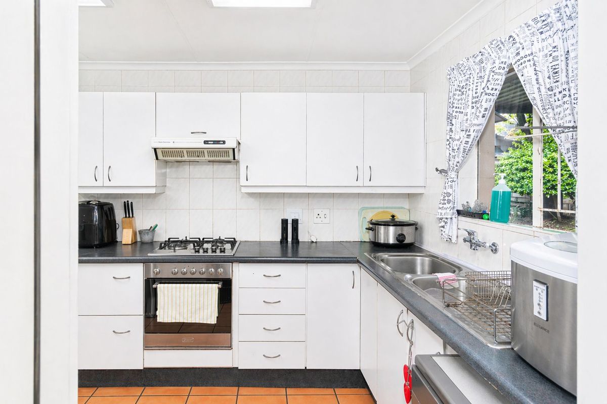 A functional kitchen featuring white cabinetry, dark countertops, a built-in gas hob, oven, extractor fan, and a double stainless steel sink.