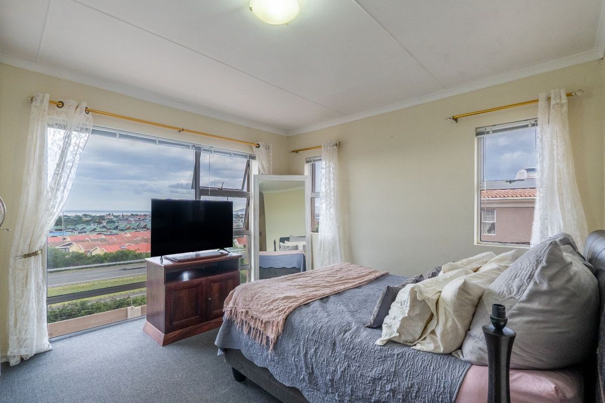 A bright bedroom featuring large windows with expansive views, neutral wall tones, and carpeted flooring.