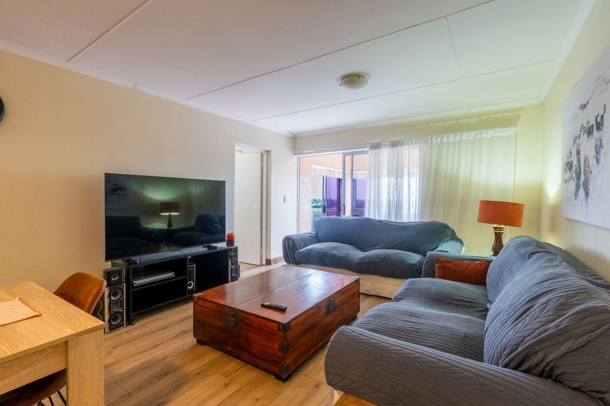 A comfortable living room featuring wood-look flooring and sliding glass doors that provide access to an outdoor balcony area.