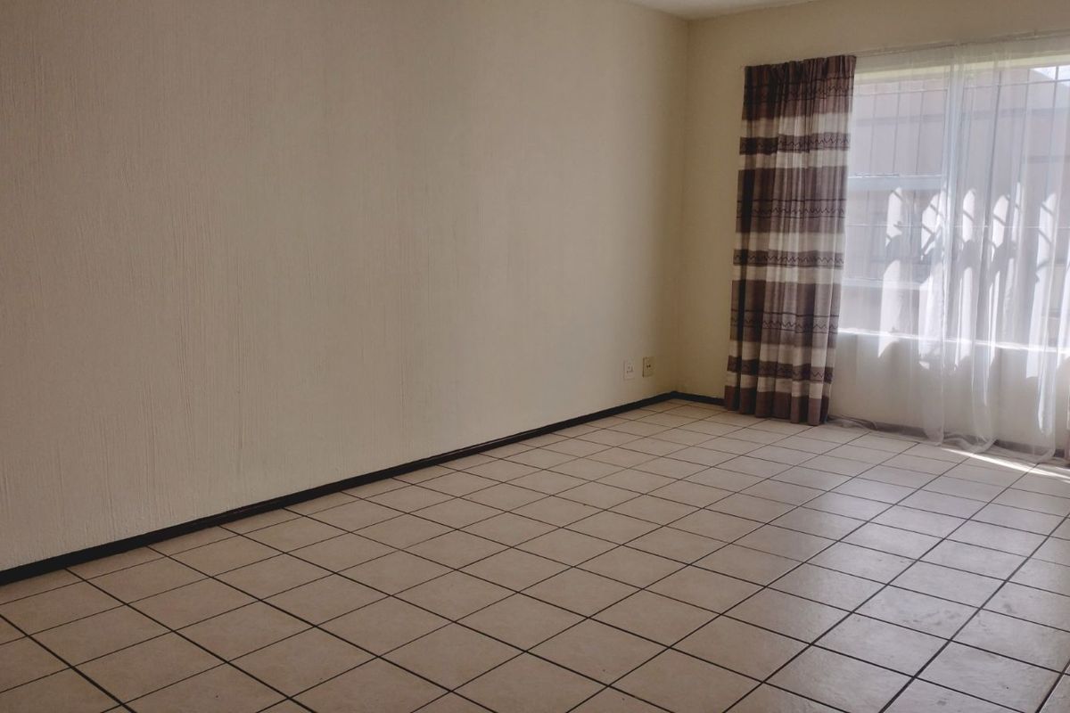 A spacious, empty living area featuring neutral tiled flooring and large windows with installed curtain tracks.