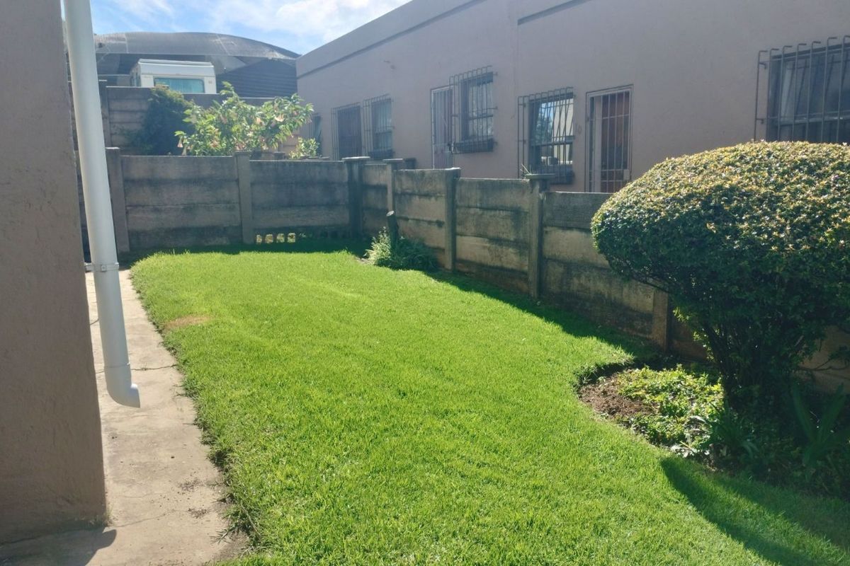 A private rear garden area featuring a well-maintained lawn, established shrubbery, and concrete boundary walling.