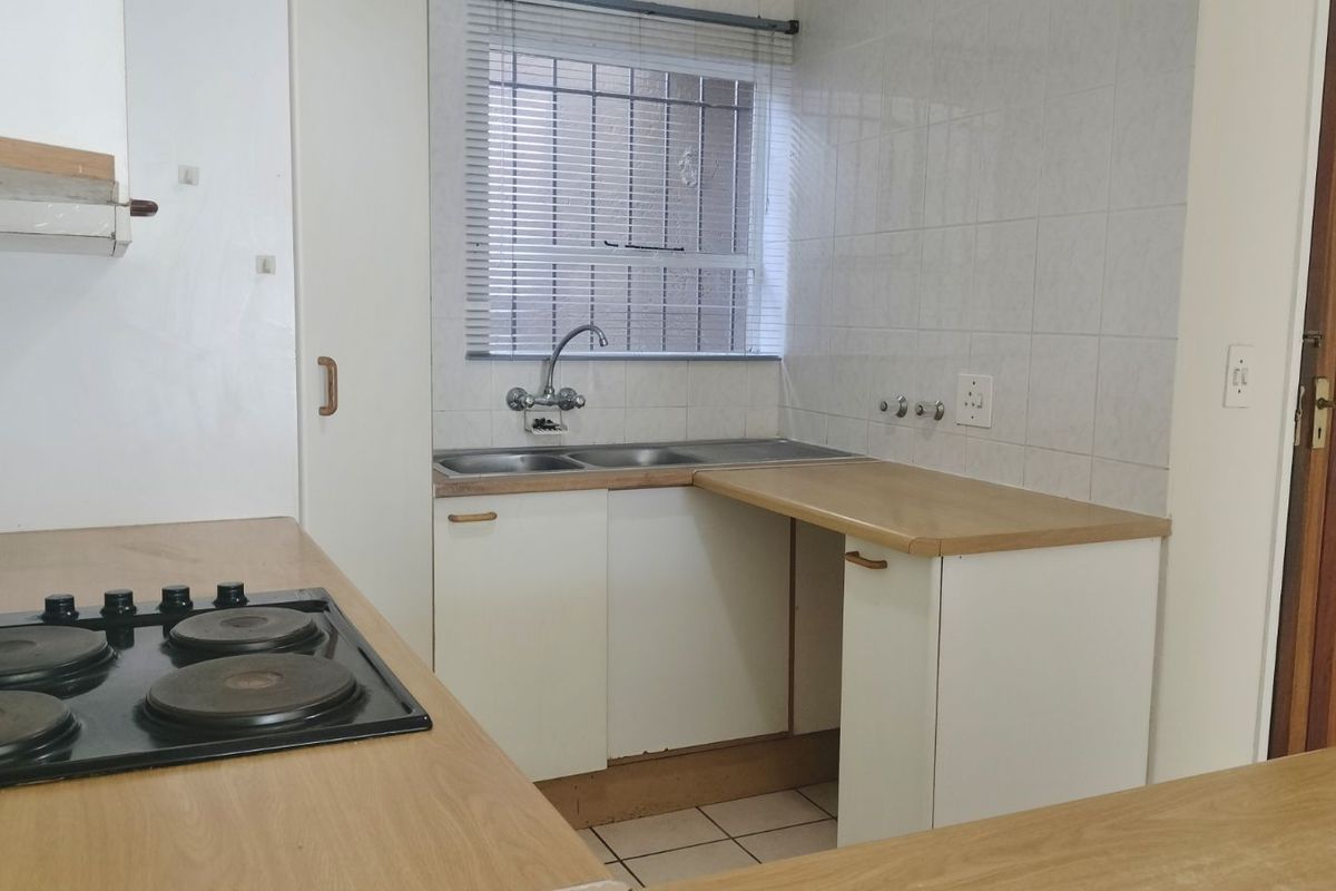 A functional kitchen featuring a built-in electric hob, double sink, tiled splashbacks, and laminate countertops with ample storage cabinetry.