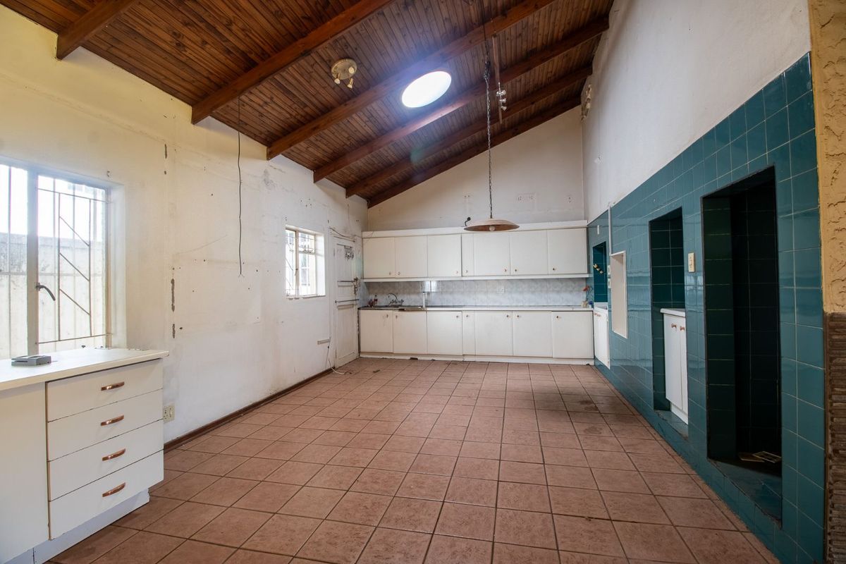 Spacious kitchen featuring a vaulted timber ceiling, skylight, white cabinetry, and tiled flooring, offering a blank canvas for renovation.