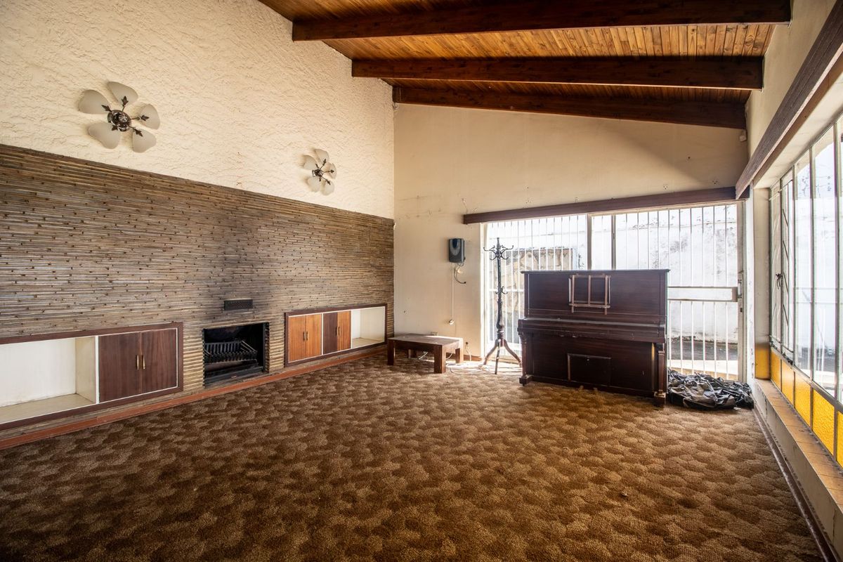 Spacious living room featuring a vaulted timber-beamed ceiling, a built-in fireplace with integrated cabinetry, and large windows with security bars.