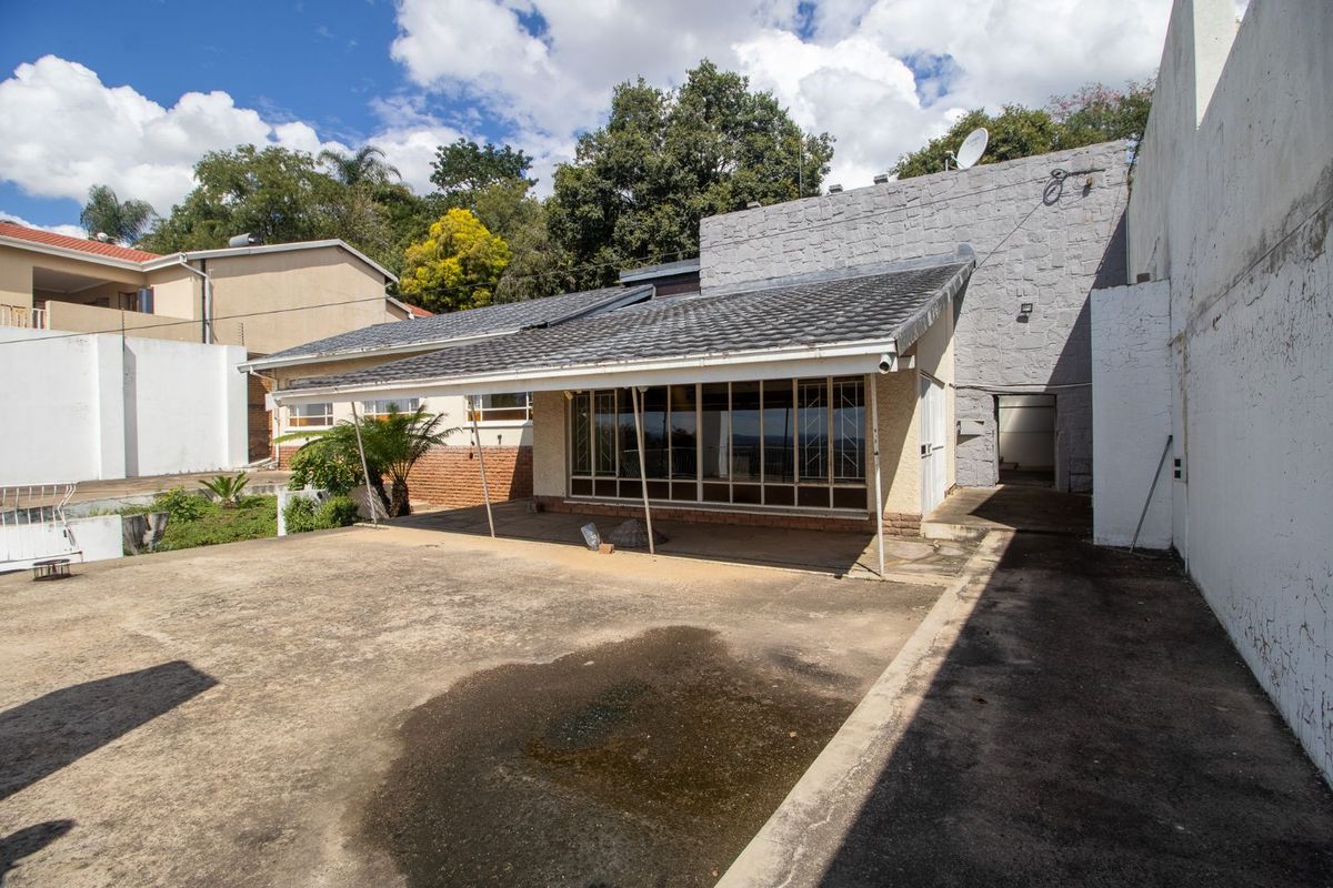 Rear exterior view of the property featuring a covered patio area, concrete paving, and a stone-clad feature wall.