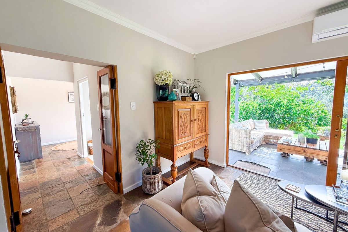 A bright living room featuring natural stone flooring, crown molding, and a large sliding door providing seamless access to a covered outdoor patio area.