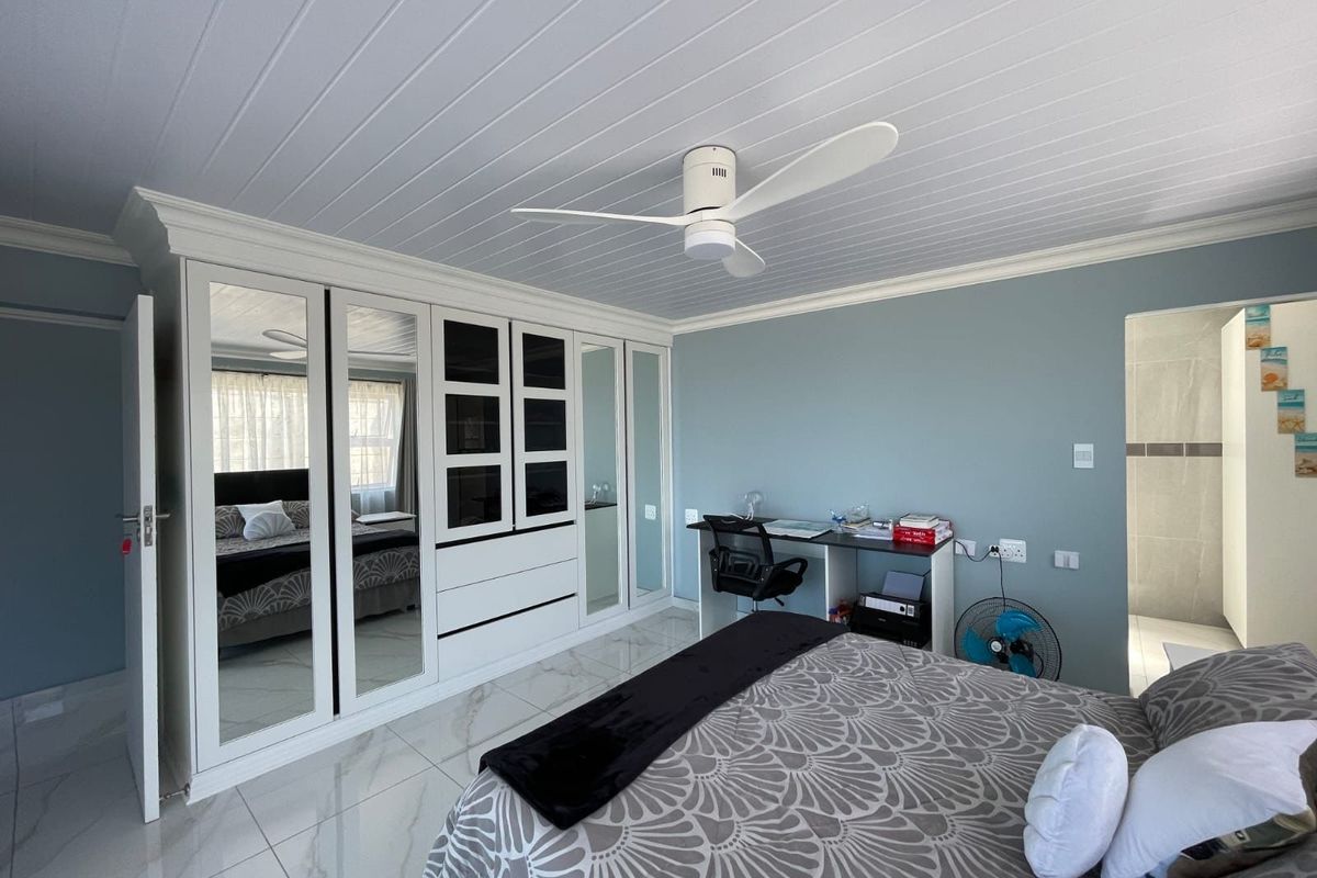 Spacious bedroom featuring modern tiled flooring, a white tongue and groove ceiling with a fitted fan, and extensive built-in mirrored wardrobe storage.