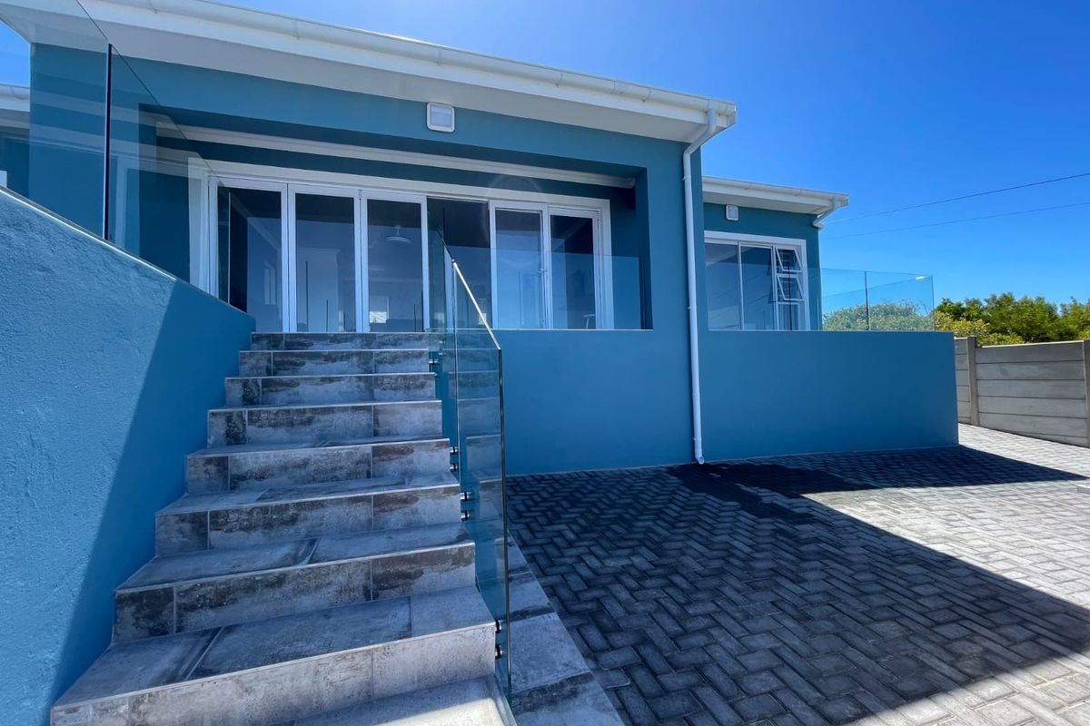 Rear exterior view featuring a modern tiled staircase with glass balustrades, paved driveway, and large sliding glass doors leading into the home.