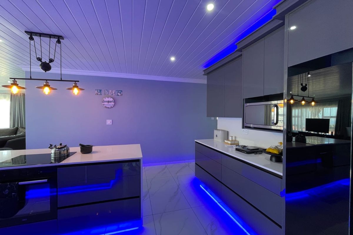 Modern kitchen featuring sleek grey cabinetry, stone countertops, integrated appliances, and ambient LED strip lighting with a contemporary tongue and groove ceiling finish.