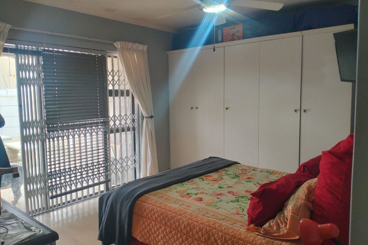 A bedroom featuring built-in wardrobes, a ceiling fan, and sliding glass doors with security gates leading to the exterior.