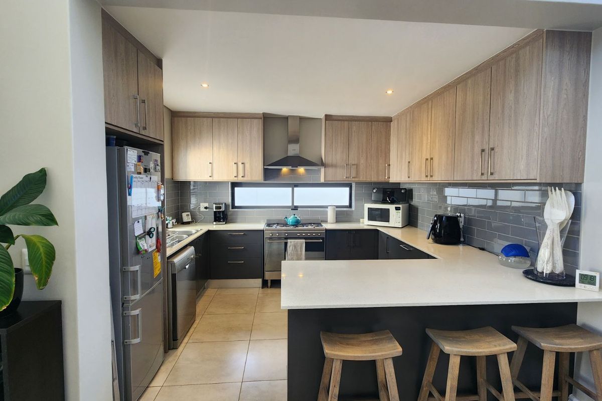 Modern U-shaped kitchen featuring light wood-tone cabinetry, stone countertops, a breakfast bar, stainless steel appliances, and a tiled backsplash.