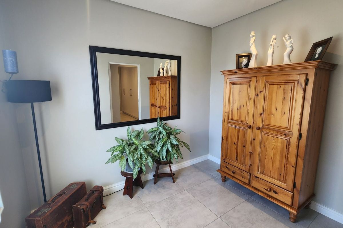 A neutral-toned living area featuring tiled flooring, a large wall-mounted mirror, and a view into an adjacent hallway.