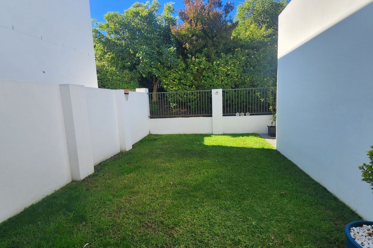 A private, enclosed rear garden featuring a well-maintained lawn, perimeter boundary walls, and metal security fencing.