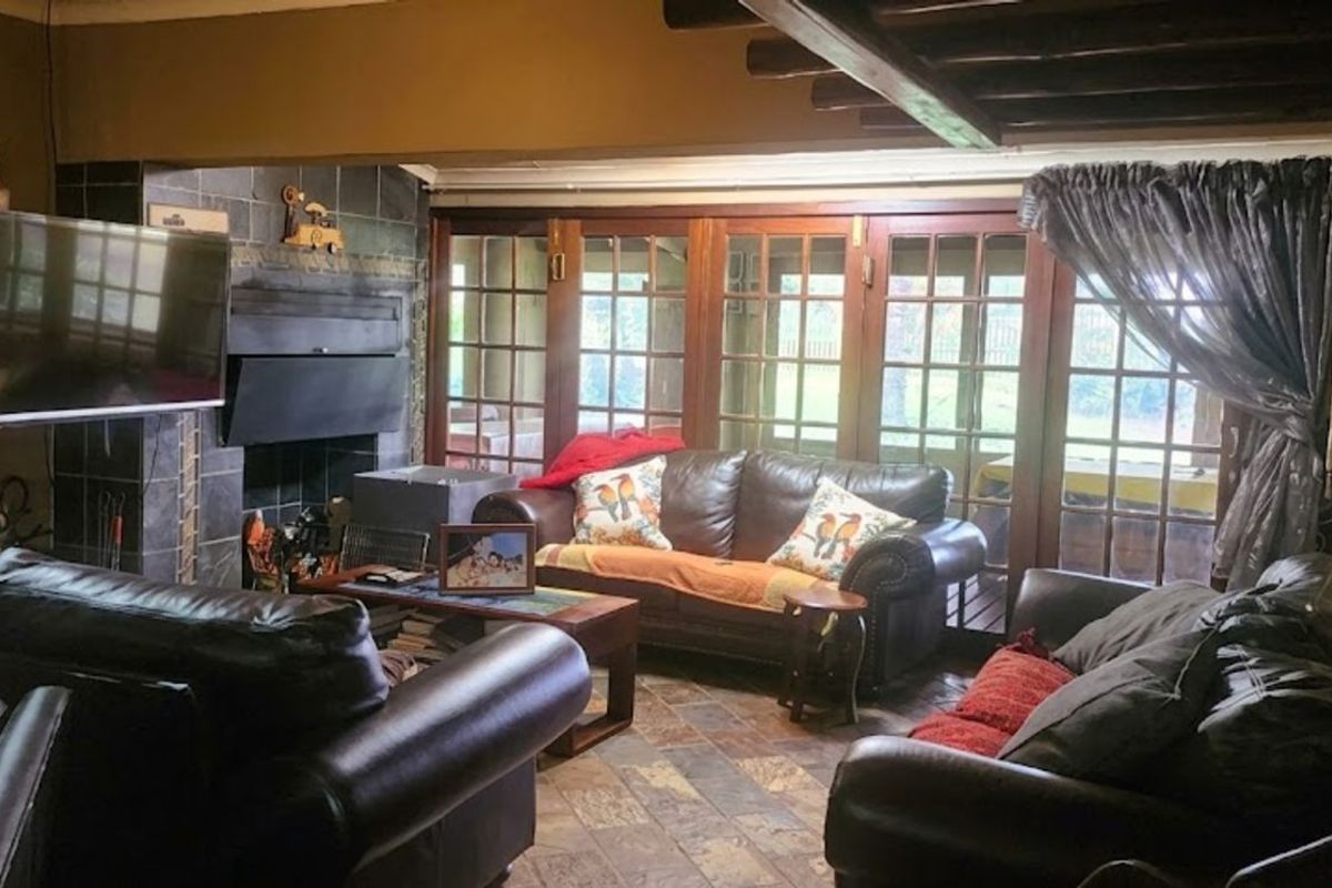 Cozy living room featuring a stone-clad fireplace, exposed timber ceiling beams, and large wooden-framed glass doors leading to the outdoor area.