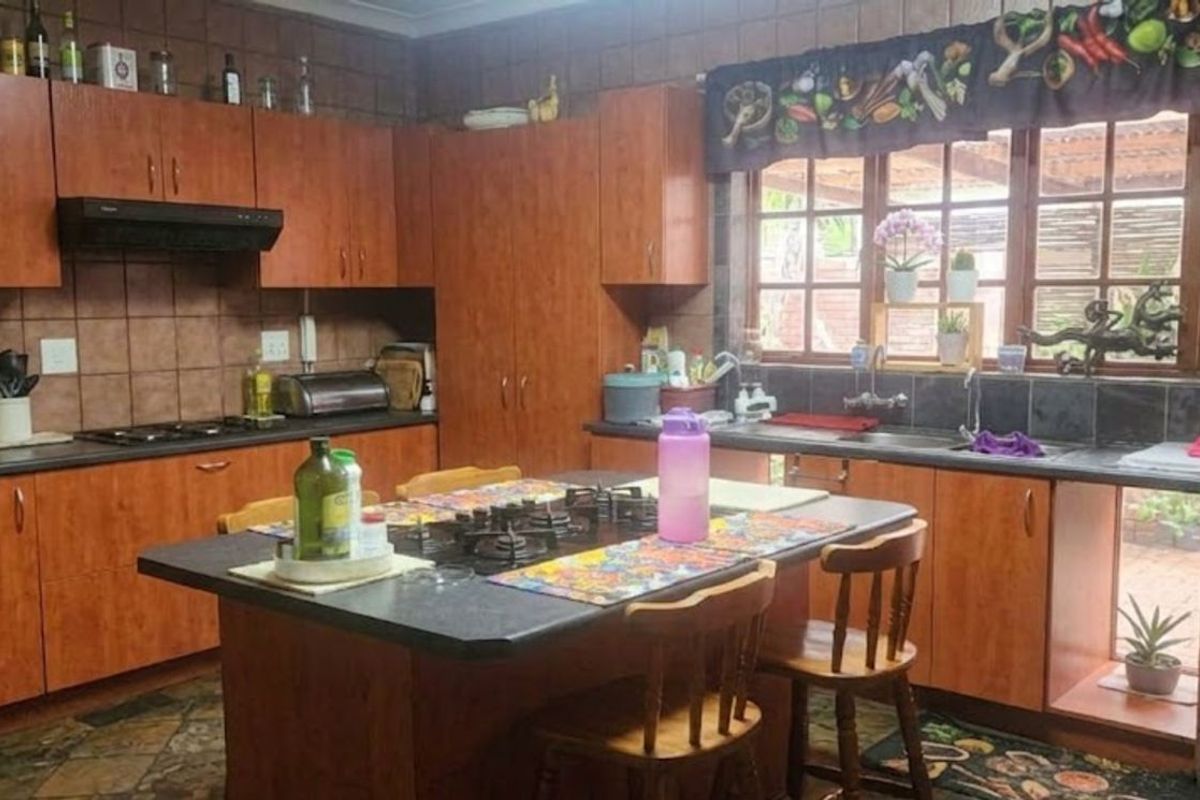 Spacious kitchen featuring wood-finish cabinetry, a central island with a built-in gas hob, dark countertops, and a tiled backsplash with garden views.