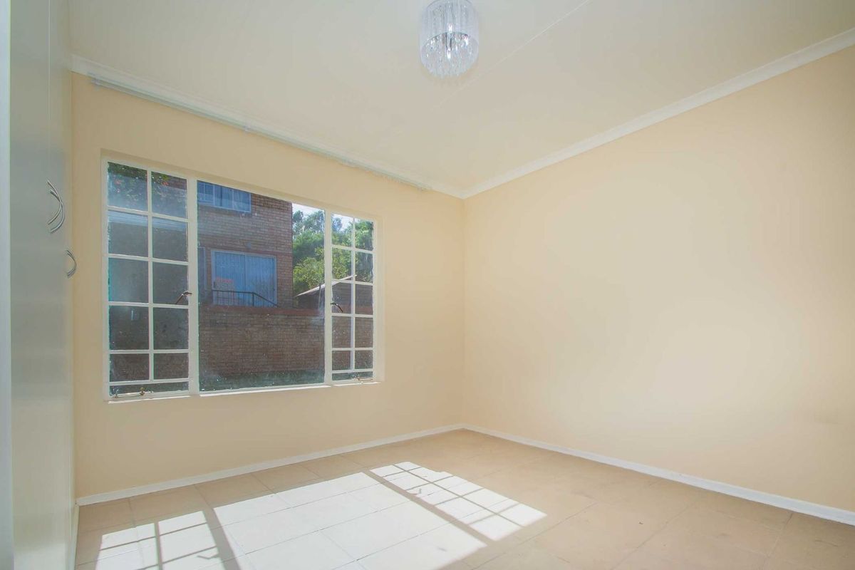 A bright, empty bedroom featuring tiled flooring, built-in cupboards, and large windows allowing for ample natural light.