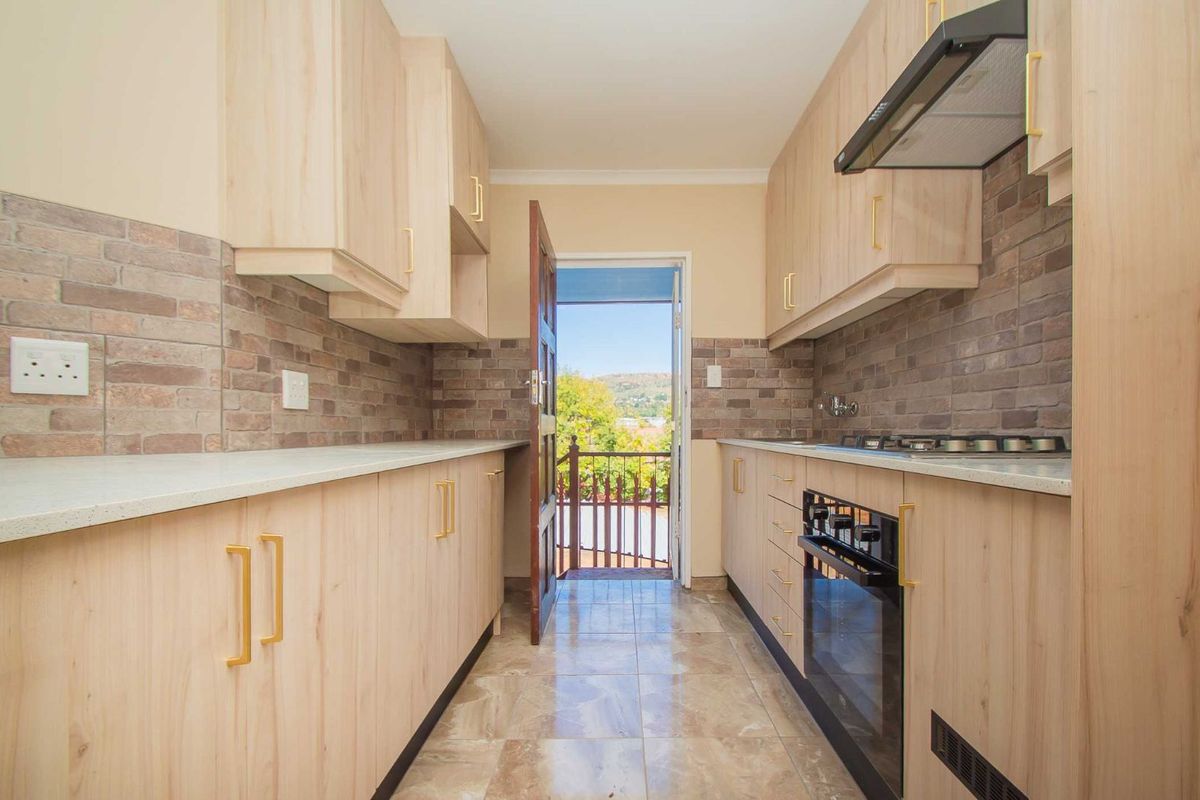 Modern galley-style kitchen featuring light wood cabinetry, stone-look countertops, brick-style backsplash, built-in oven, gas hob, and extractor fan with direct balcony access.