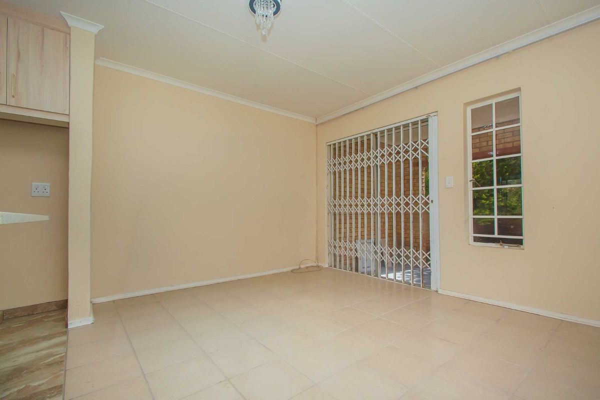 An empty living area featuring tiled flooring, a security gate leading to the exterior, and a window with security bars.