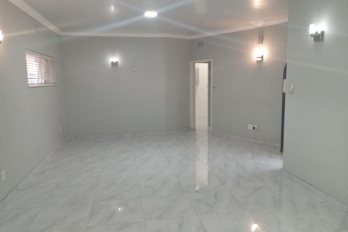 A spacious, empty living area featuring modern light-colored marble-look floor tiles, recessed ceiling lighting, and wall-mounted sconces.