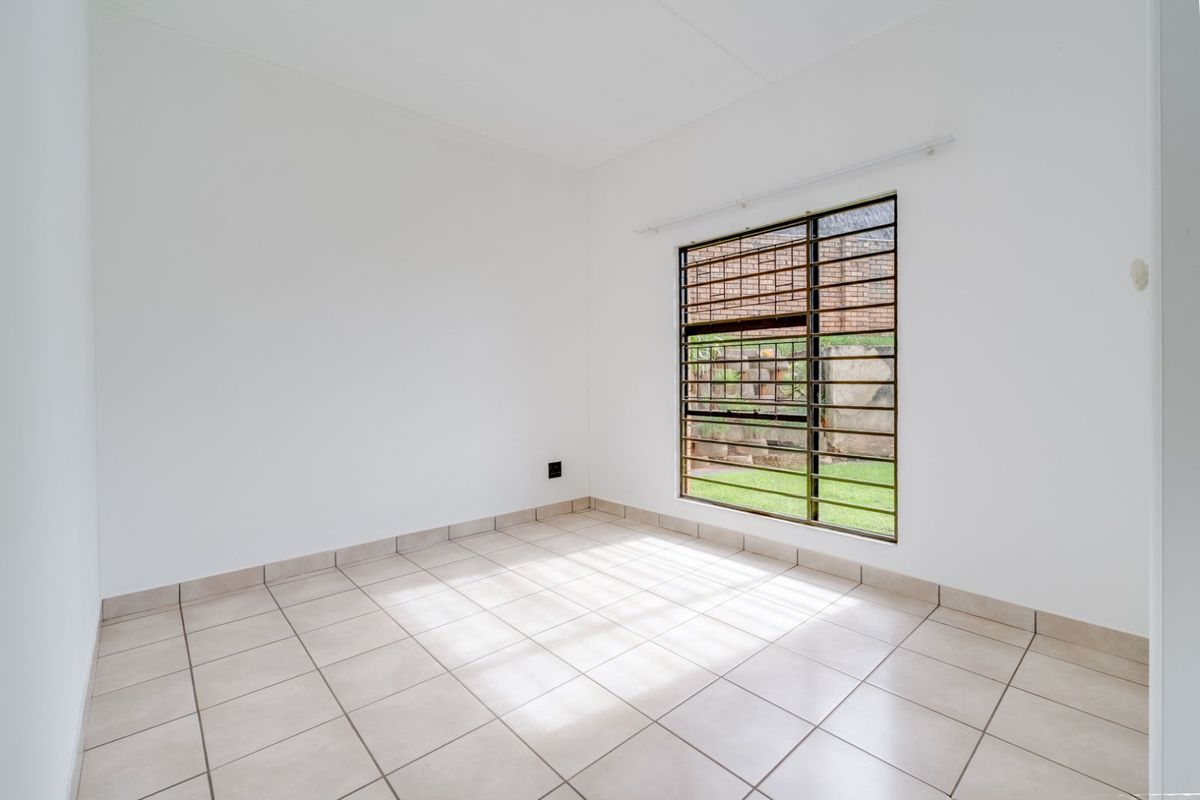 A bright, empty bedroom featuring neutral floor tiles and a large window fitted with security bars, offering a clean and versatile living space.