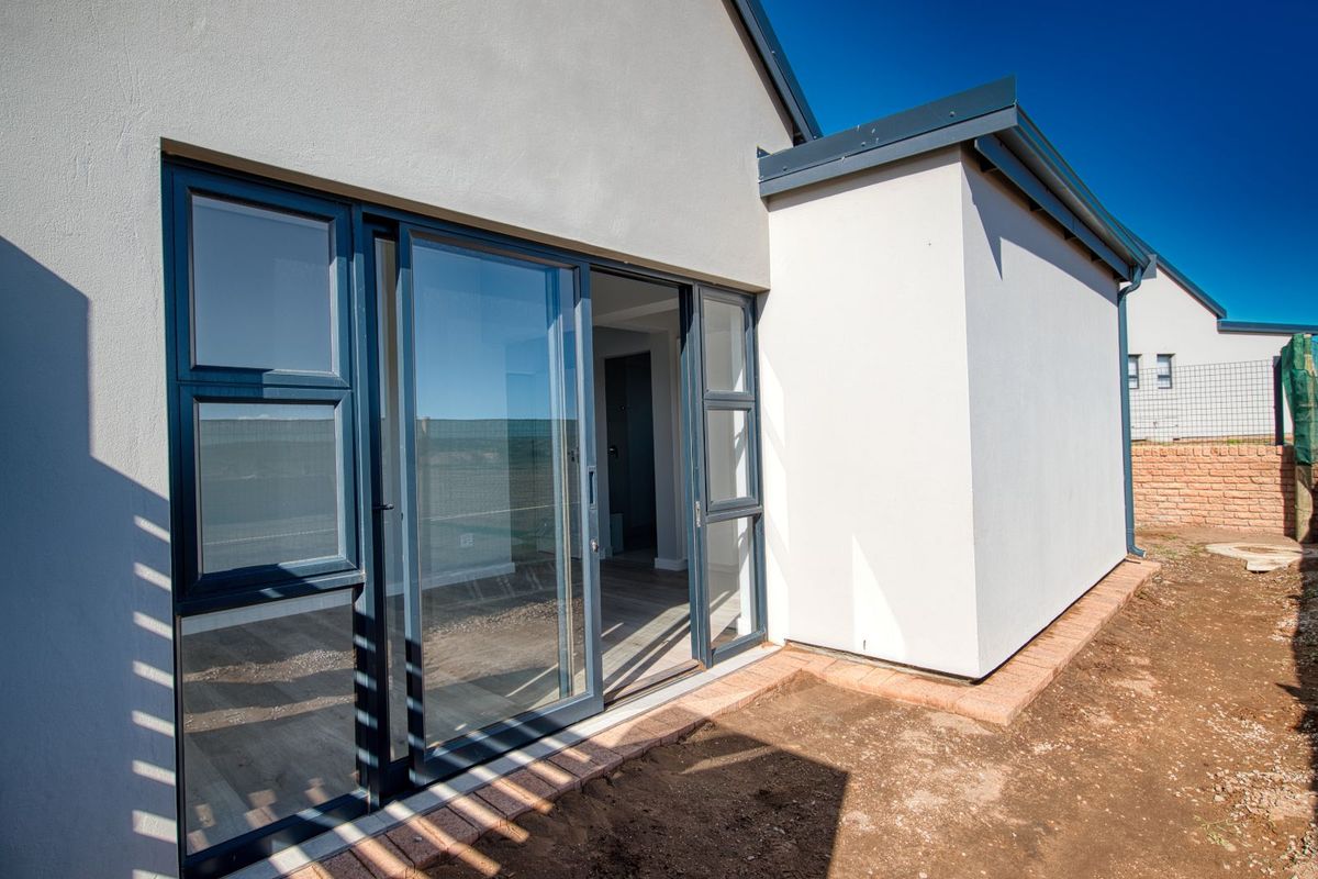 Rear view of the property featuring modern dark-framed sliding glass doors leading into the interior, with an unfinished garden area.